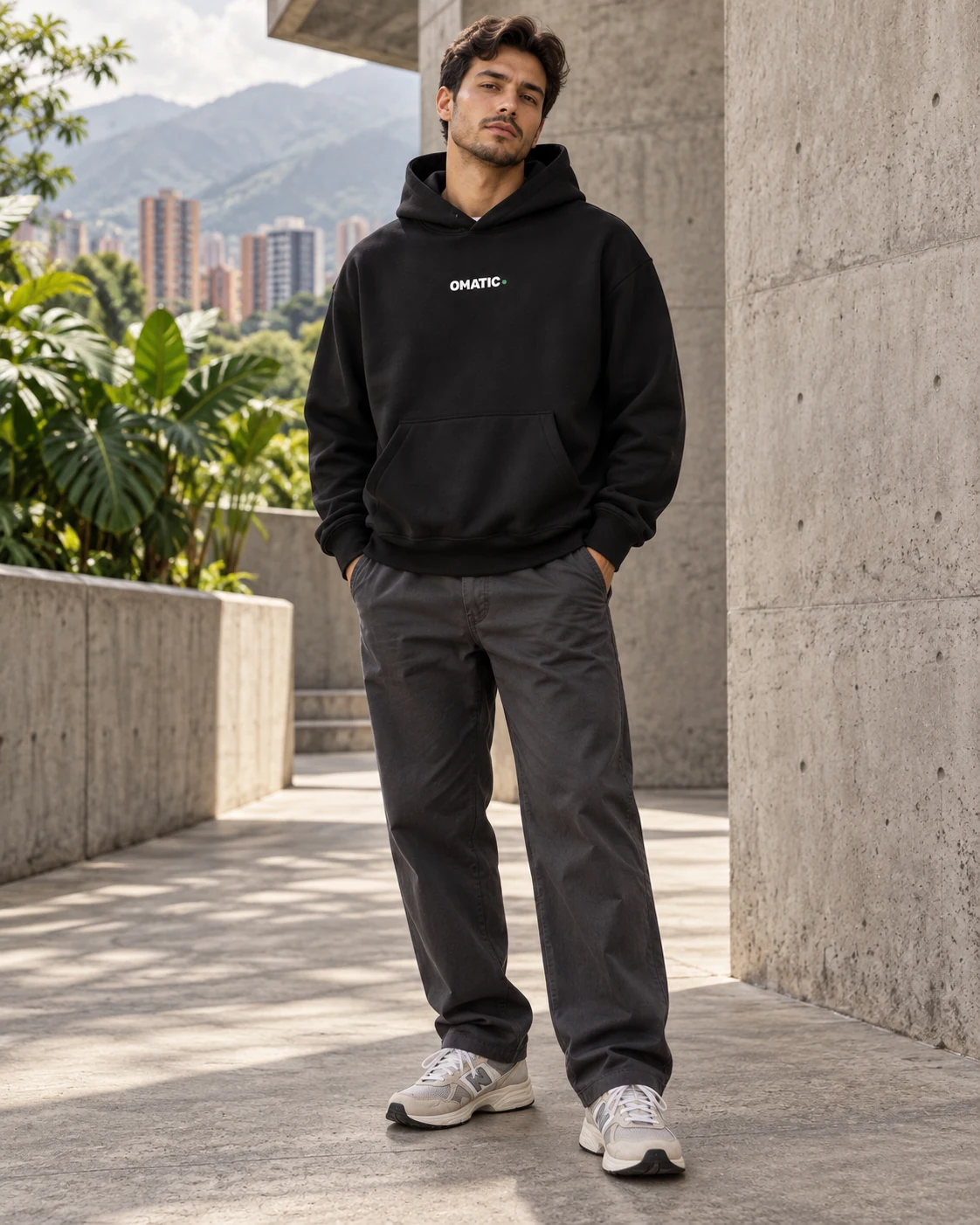 Modelo con OMATIC Core Hoodie negro, logo blanco al frente y pantalón gris oscuro